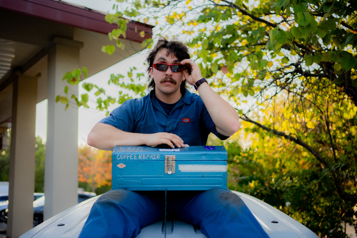 Jake Bristol, sitting on top of his service van, with a coffee repair toolkit in his lap and sunglasses on his face.