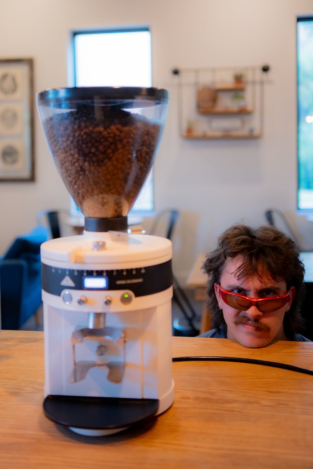 Jake Bristol of Cold Spell Coffee Services, standing between a coffee grinder, smiling with sunglasses on.
